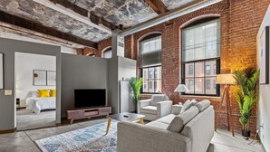 A spacious living room with a large sofa, a flat-screen TV, and a patterned rug. - Historic Loft Retreat With Pool (Pittsburgh)