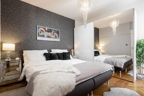 Relax in this serene bedroom with a large bed, nightstands, and a mirror, surrounded by a textured pattern and a beautiful piece of artwork.