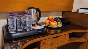 Een hotel bureau met een waterkoker, waterflesjes, een schaal met fruit en een telefoon.