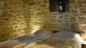 A stone-walled room with a bed featuring patterned bedding and a small window with a figure. - Room in Studio - Enchanting Escapade in Krsuli (Sveti Lovrec)