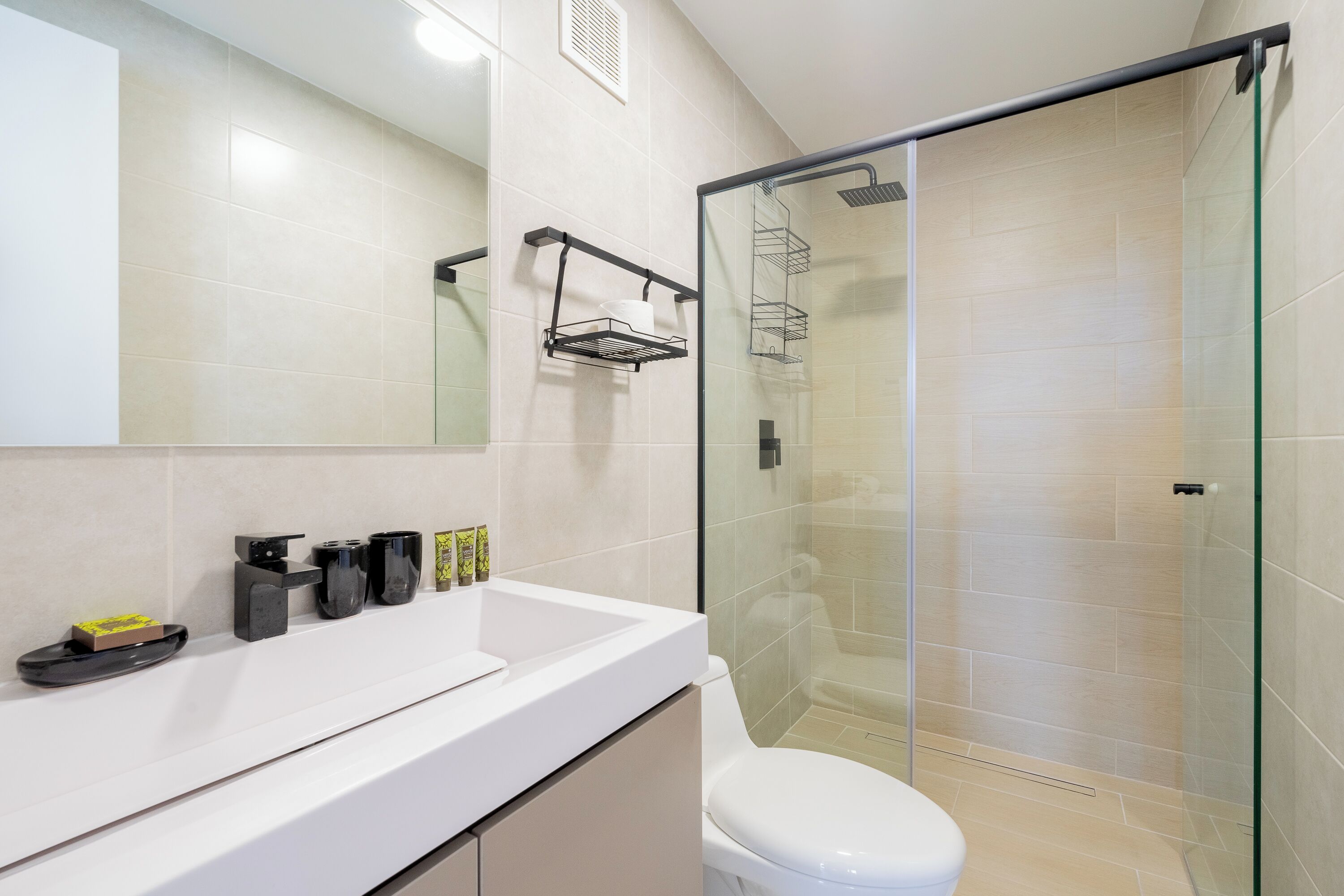 Une salle de bain avec un lavabo blanc, des toilettes, une douche en verre et un miroir.