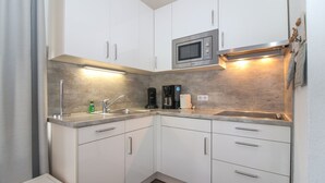 A compact kitchen with white cabinets, a stainless steel sink, a microwave, and a coffee maker.