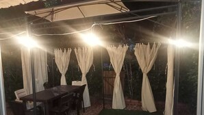 A covered outdoor seating area with a table and chairs, surrounded by curtains and string lights. - Casa de Verano Mediterranea (Carmen de Apicalá)