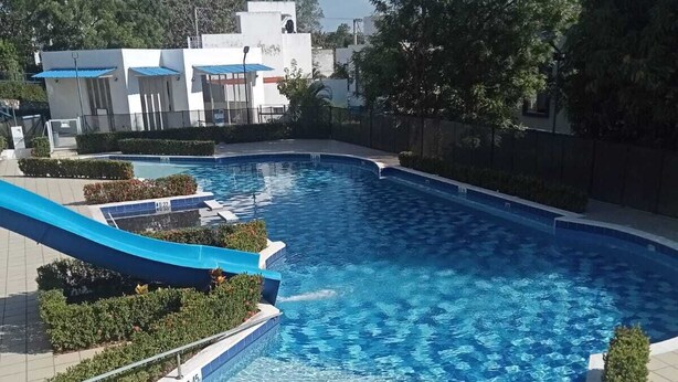 A swimming pool with a blue slide, surrounded by greenery and modern buildings. - Casa de Verano Mediterranea (Carmen de Apicalá)