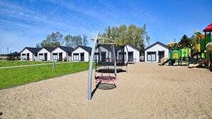 A playground with swings and a slide, surrounded by white houses with dark roofs. - Cozy holiday homes, close to the lake (Lazy)