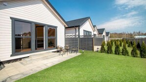 A modern house with a patio, a lawn, and a row of evergreen trees. - Cozy holiday homes, close to the lake (Lazy)