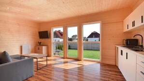 A modern interior with a wooden ceiling, a sofa, a table, a kitchen area, and large sliding glass doors leading to a backyard. - Cozy holiday homes, close to the lake (Lazy)