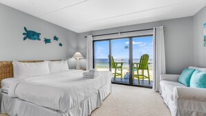 Ett hotellrum med en stor säng, en soffa, en grön fåtölj och utsikt över stranden genom en skjutdörr.