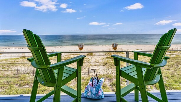 Två gröna Adirondack-stolar placerade framför en strand, med en klar himmel i bakgrunden.