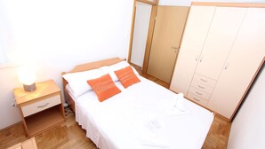 A neatly made bed with white and orange bedding, a bedside table with a lamp, and a wardrobe with multiple drawers. - Apartment Mladen (Pula)