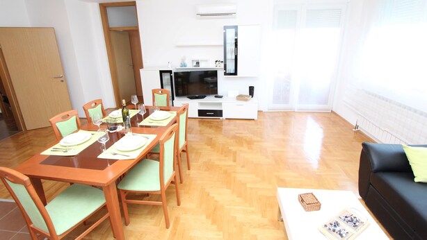 A dining area with a wooden table set for four, a black sofa, and a white coffee table with a book and a box. - Apartment Mladen (Pula)