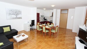 A modern living room with a black sofa, a white coffee table, and a dining area with a wooden table and chairs. - Apartment Mladen (Pula)