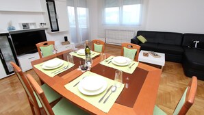 A dining area with a wooden table set for four, surrounded by chairs. A black sofa and a small white table with a book are visible in the background. - Apartment Mladen (Pula)