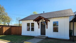 A single-story house with a front porch, a dark front door, and a small front yard with a concrete path leading to the door. - Blanche's Bungalow (Graham)