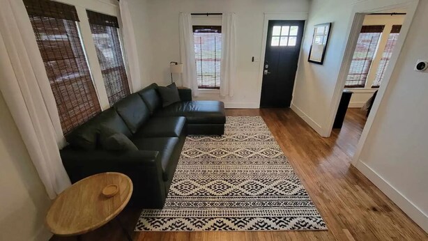 A living room with a black sectional sofa, a patterned rug, and a small wooden table. - Blanche's Bungalow (Graham)