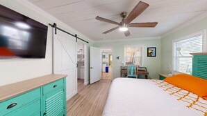 Un dormitorio con cama, escritorio, silla, ventilador de techo y puerta que da a un baño.