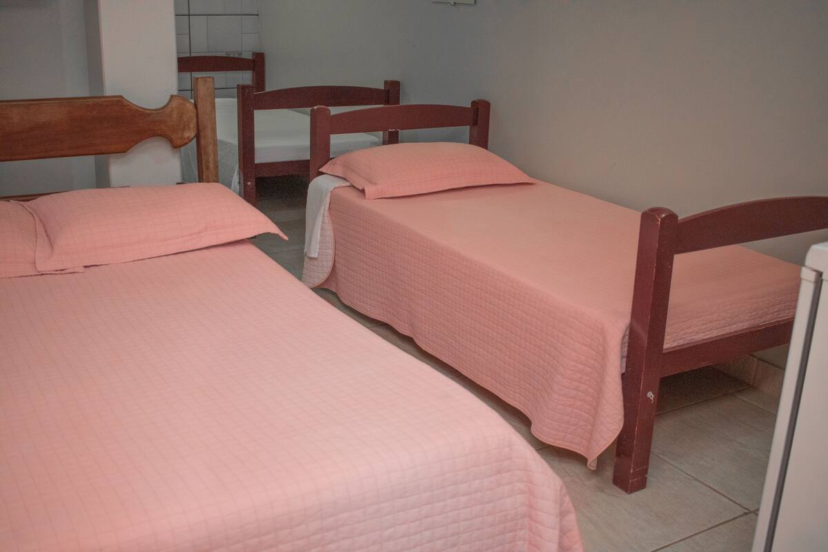 A room with two wooden beds, each with a pink quilted bedspread and matching pillows.