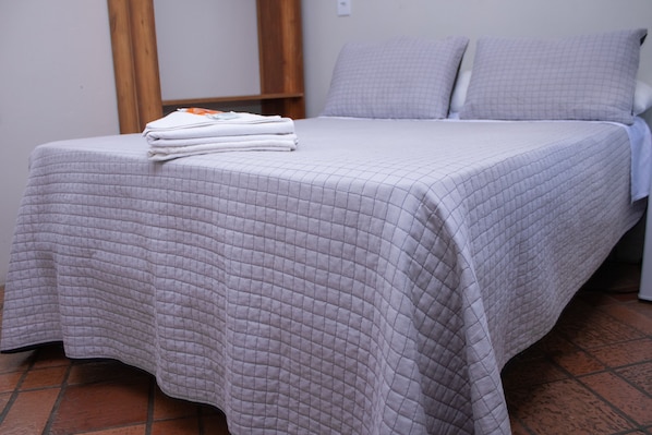 Un lit bien fait, avec une couvre-lit matelassé et des oreillers, une table de chevet en bois et un sol carrelé.