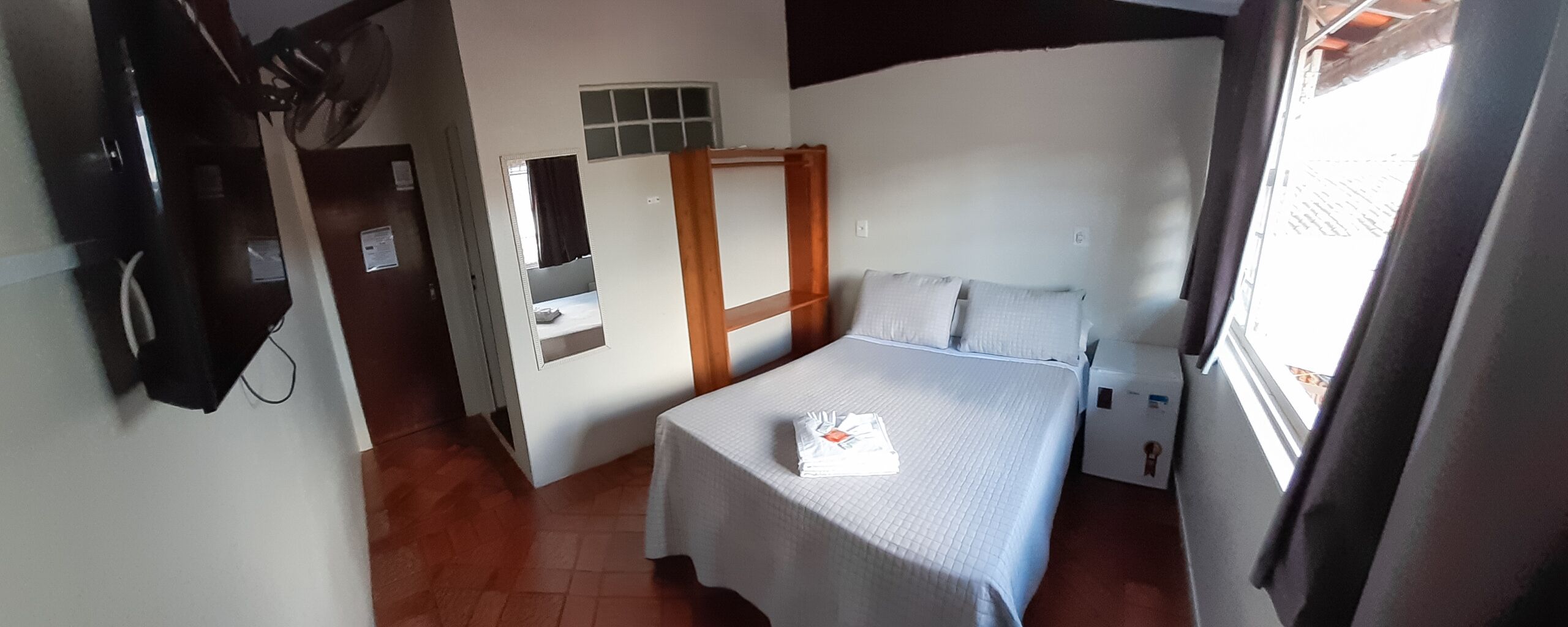 Une petite pièce, de taille modeste, comprenant un lit, une petite table, un miroir et une fenêtre.