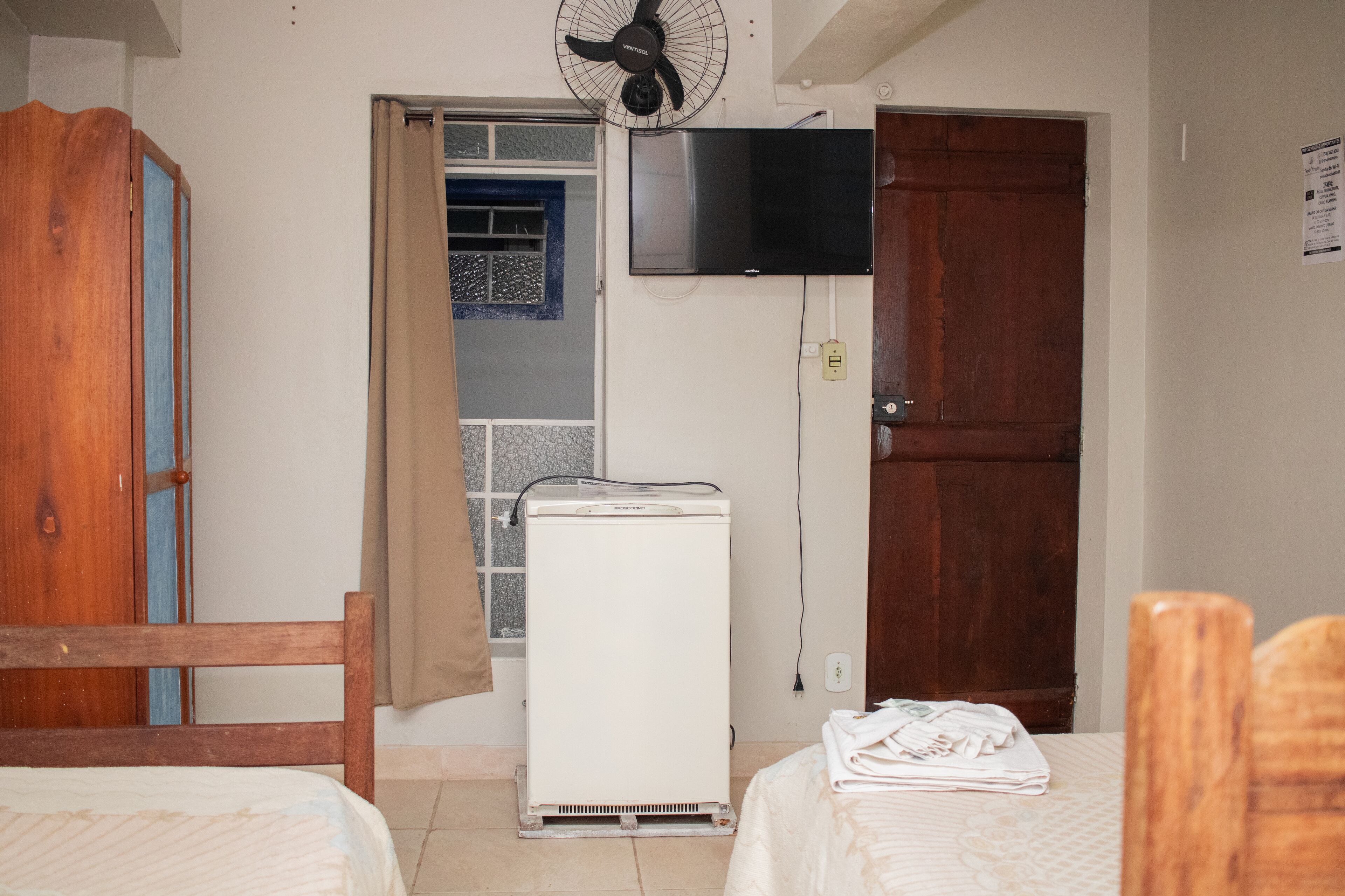 A room with a bed, a heater, a TV mounted on the wall, and a wooden door.