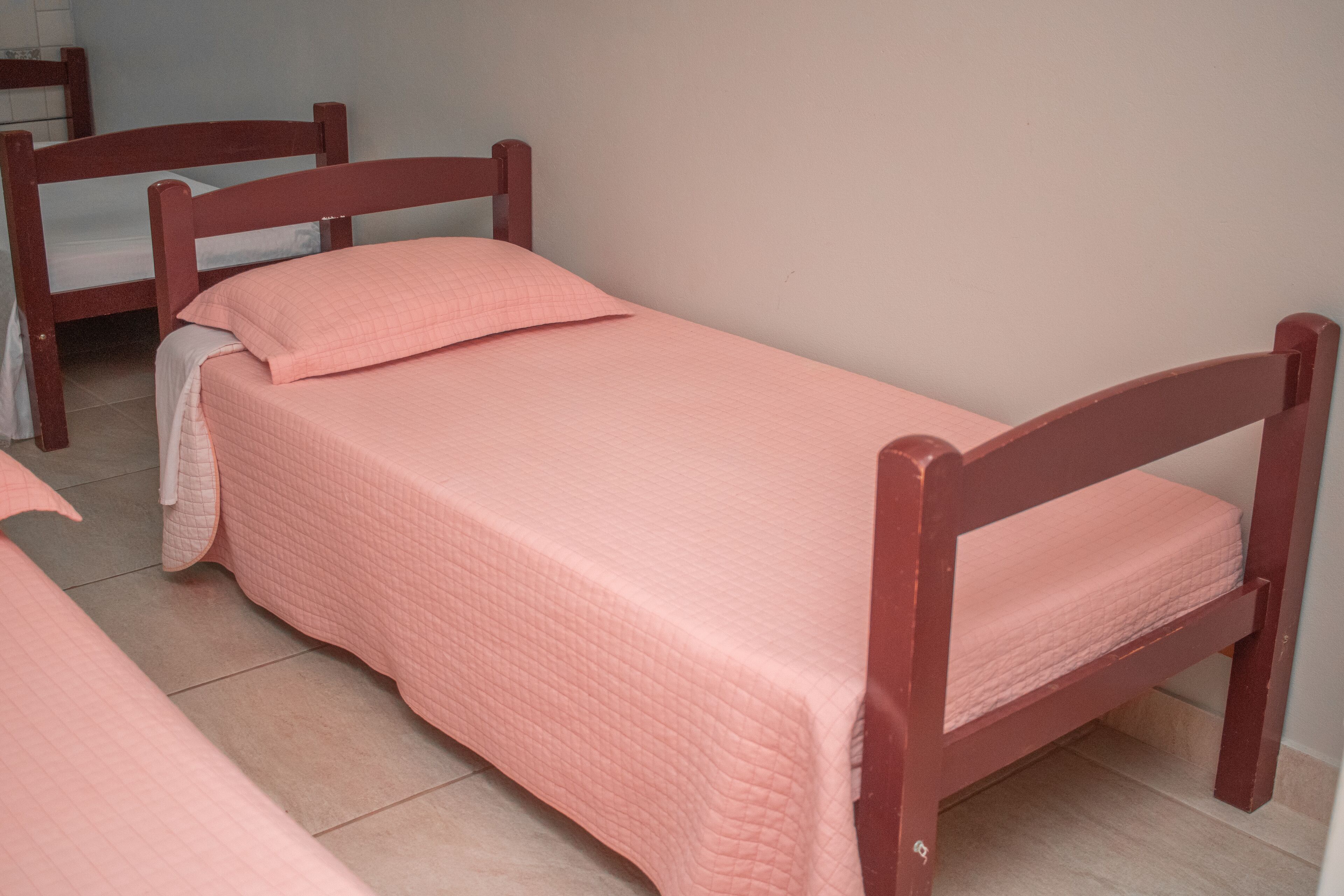 A small, single-bed room with a wooden frame and a pink quilted bedspread.