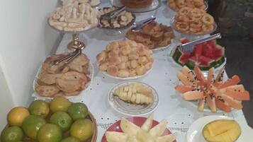 A buffet table with various food items including fruits, pastries, and bread.