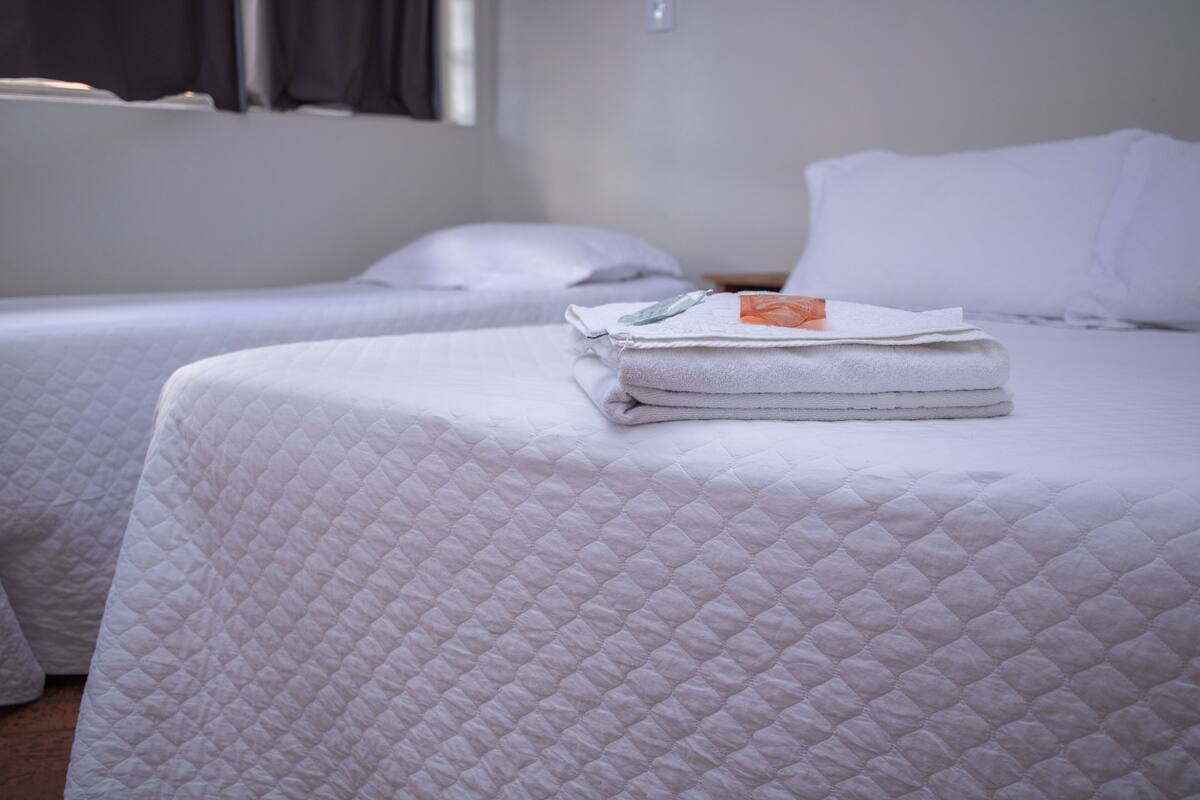 A hotel room with two beds, each with a white quilted bedspread and neatly folded white towels.