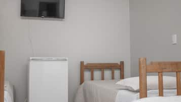 Un dormitorio con cama, cabecero de madera, mesita de noche blanca y televisor instalado en la pared.