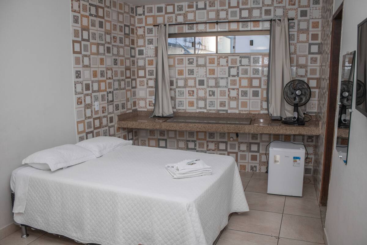 A small, clean room with a bed, a small sink, and a refrigerator.