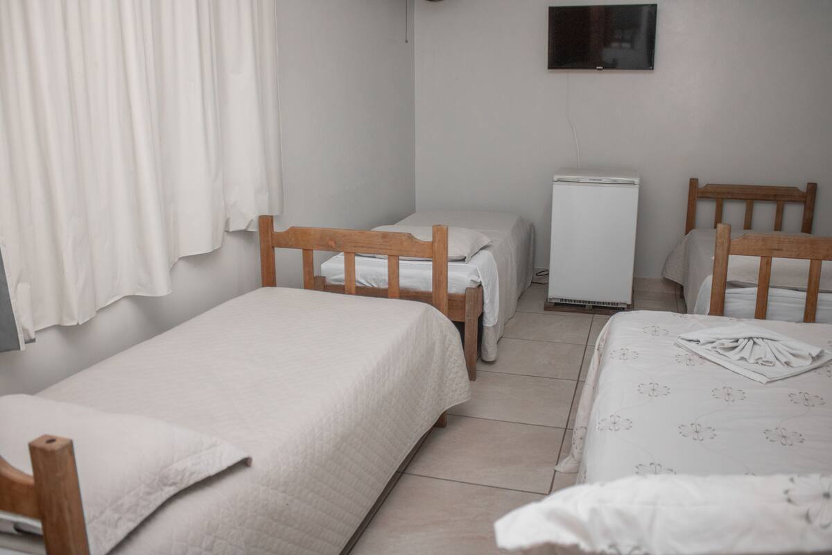 A small, clean room with two single beds, a small white refrigerator, and a TV mounted on the wall.