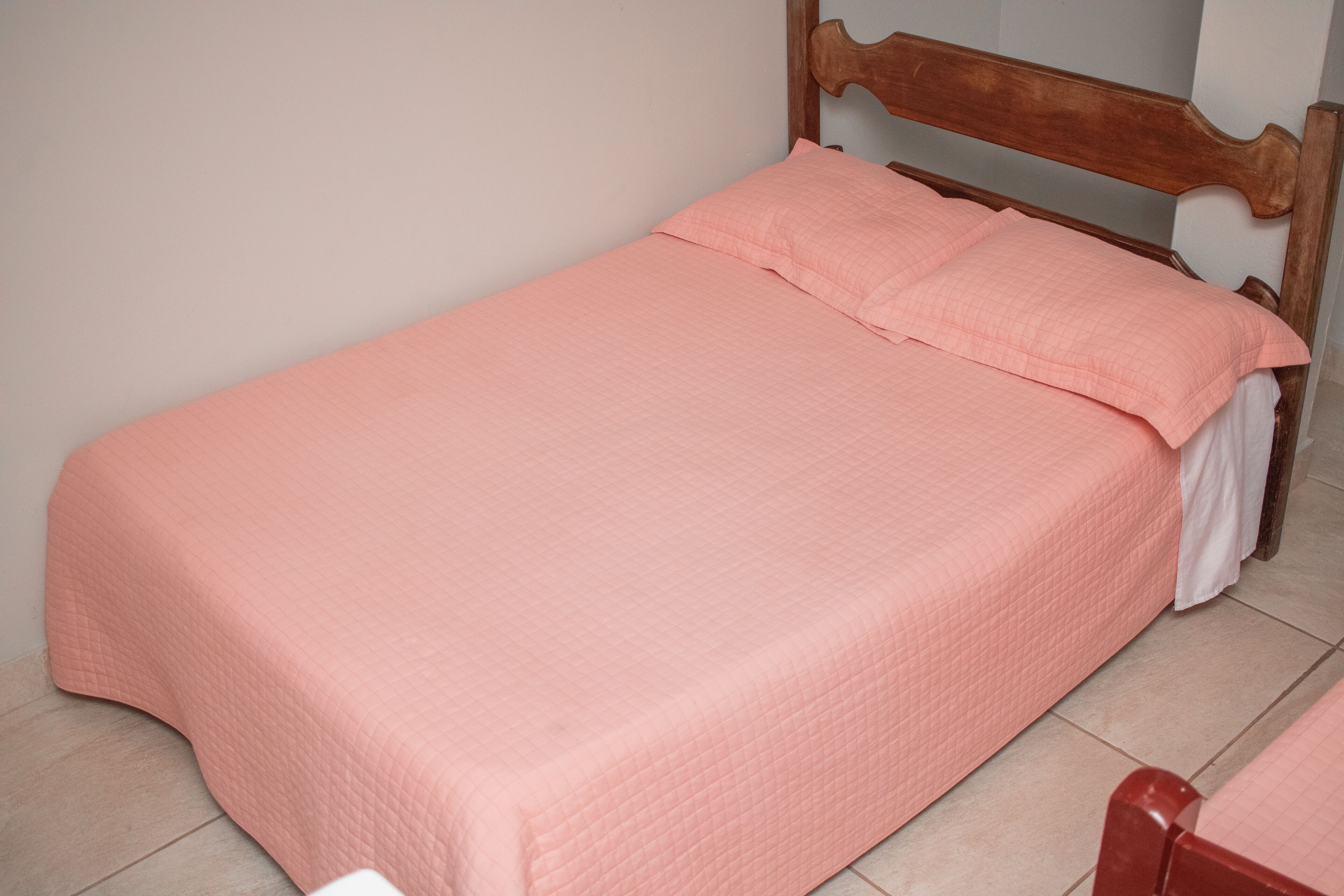 Una cama individual con cabecera de madera y colcha acolchada rosa.