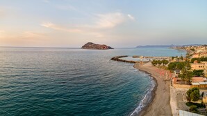 A coastal view with a rocky island, a sandy beach, and a pier extending into the sea. - Platanias Beachfront Villa Elsa-90m to main Square (GW95+FMM Platanias, Greece)