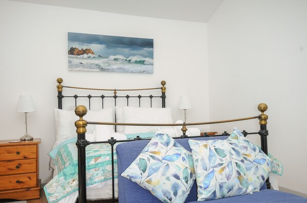 Un lit avec une tête de lit bleue, des oreillers blancs et un tableau représentant un paysage côtier au-dessus.