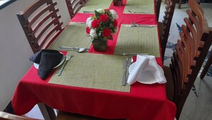 Ein Esstisch ist mit roten Tischdecken, grünen Platzsets und floralen Tischdekorationen gedeckt.