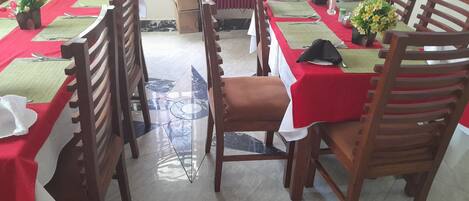 Comedor con mesas dispuestas para cuatro, cada una con mantel rojo, sillas de madera y centros de mesa con flores.