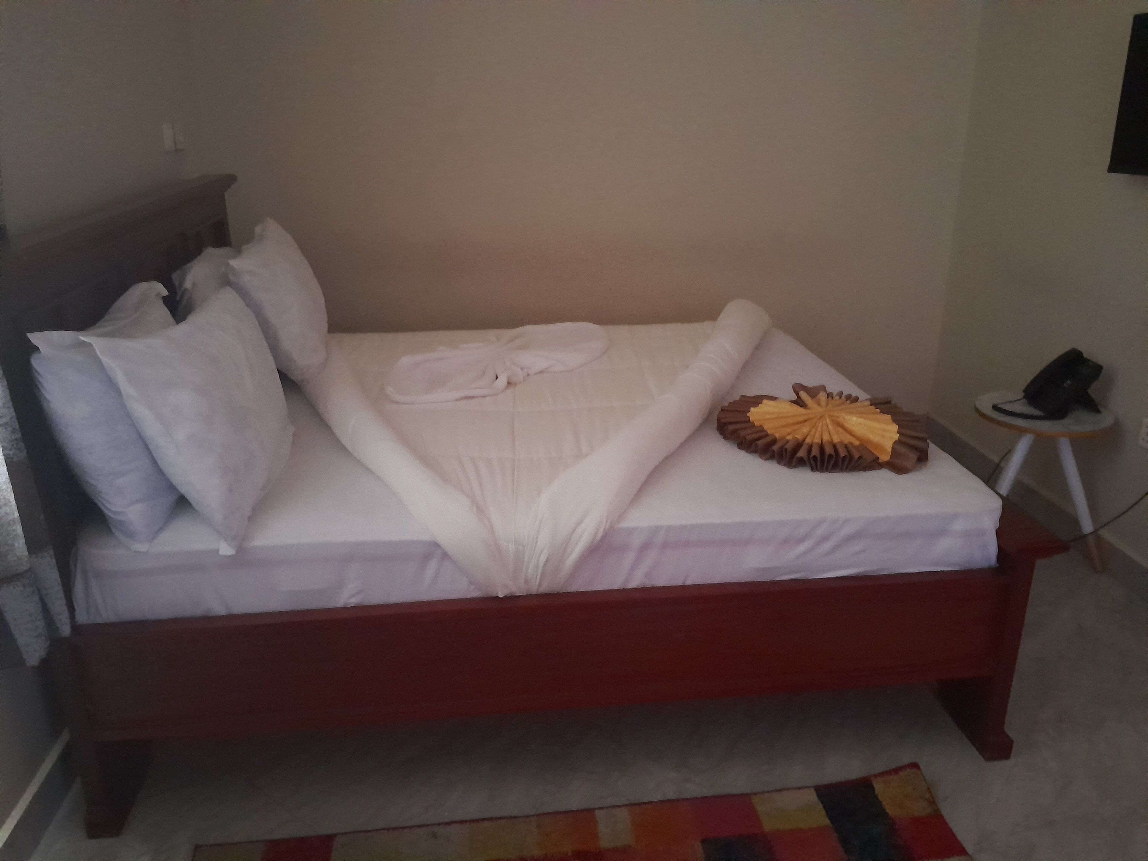 A neatly made bed with white linens, a folded towel, and a decorative fruit arrangement.
