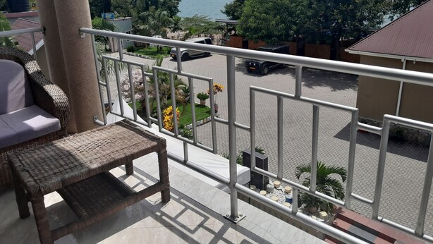 Ein Balkon mit Rattan-Sofa und Glastisch, mit Blick auf einen Parkplatz und einen See mit Bergen im Hintergrund.