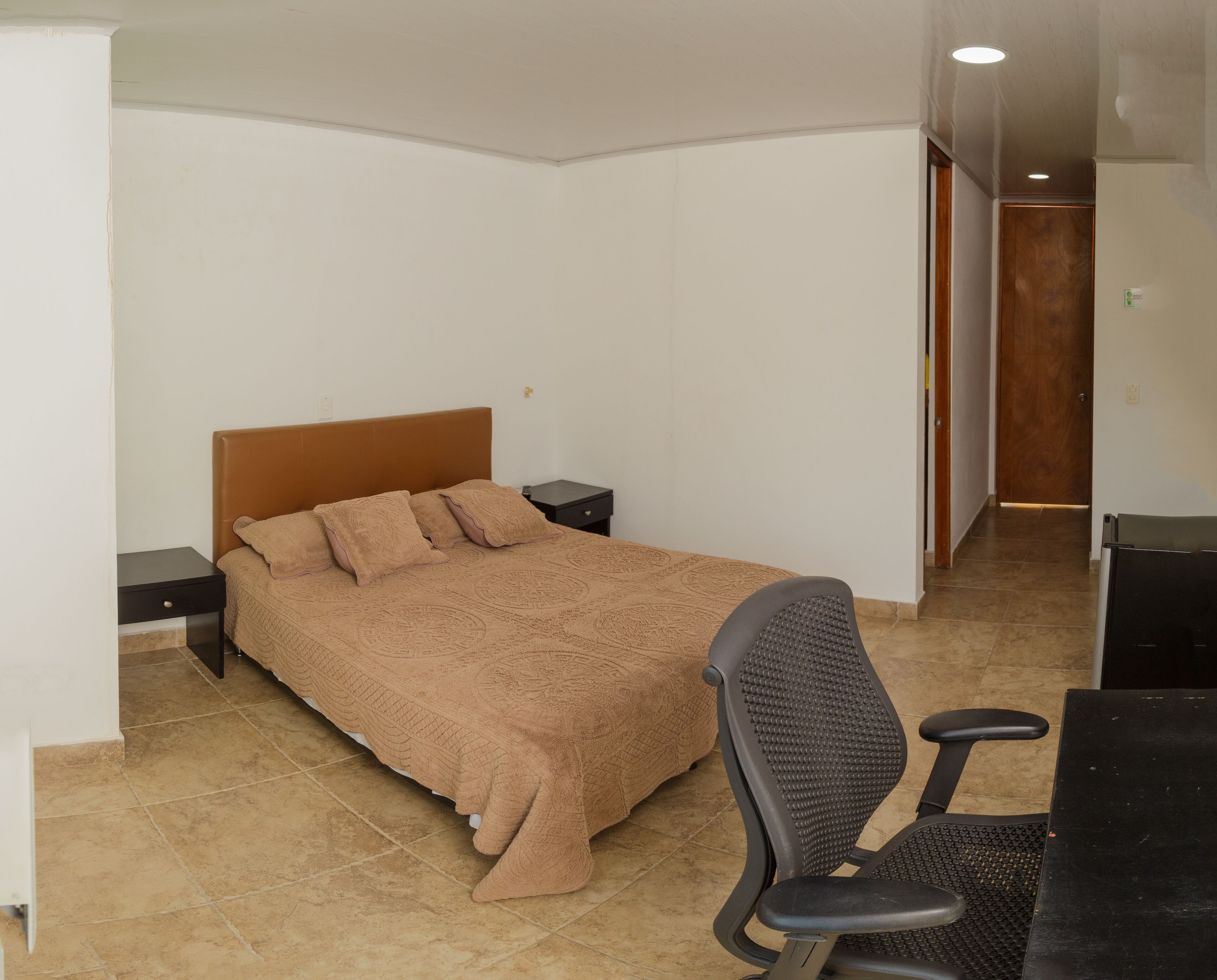Un dormitorio con una cama, dos mesitas de noche, una silla y un escritorio.
