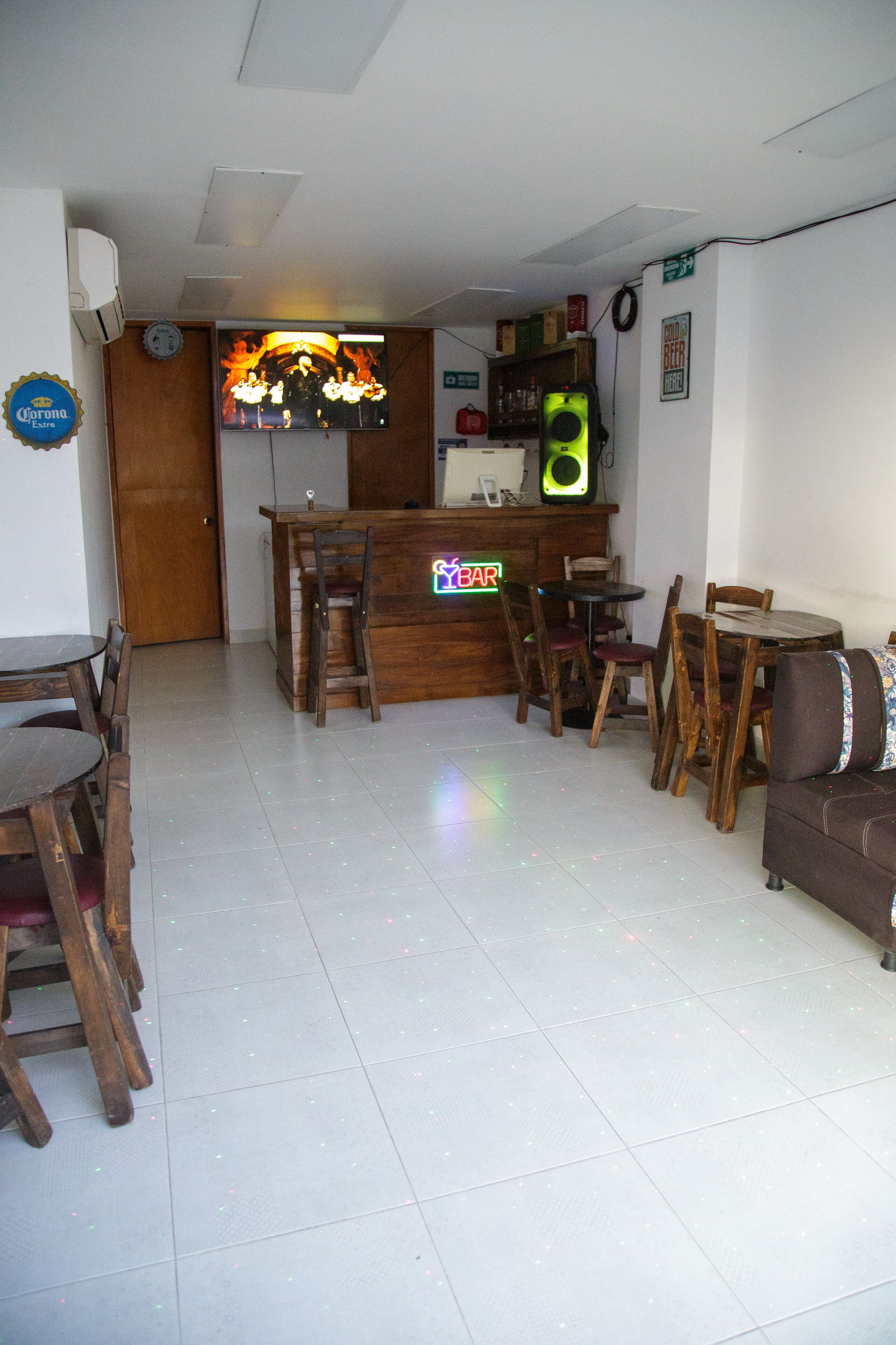Zona de bar con muebles de madera, un televisor y un letrero de neón.