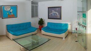 Ein modernes Wohnzimmer mit zwei blauen Sofas, einem Glastisch und einem Topfpflanzen.
