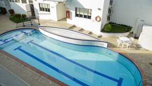 Ein Schwimmbecken mit gefliestem Sonnendeck, einem Rettungsring und einer kleinen Gartenanlage mit Stühlen.