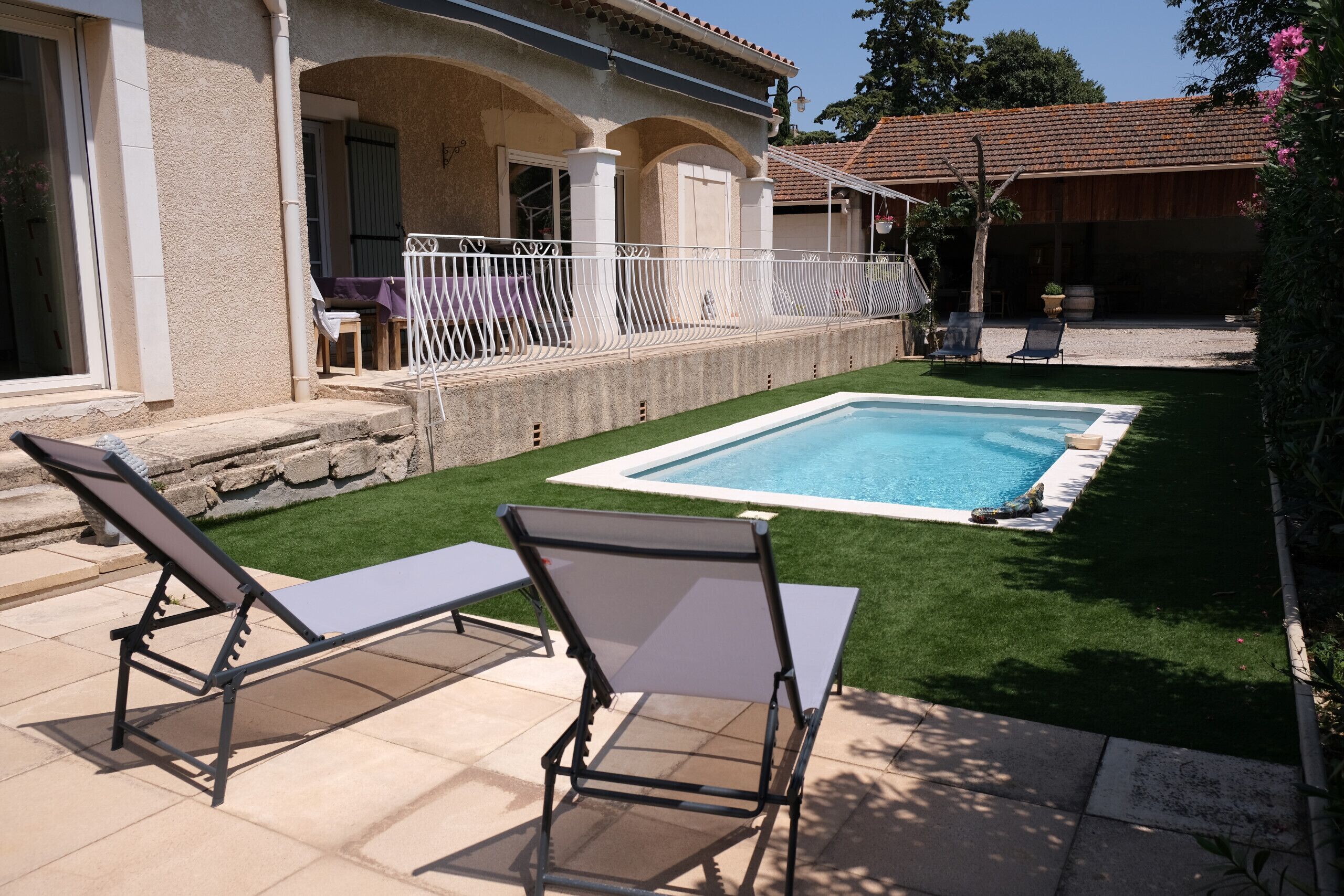 A poolside area with two lounge chairs, a small table, and a white fence.