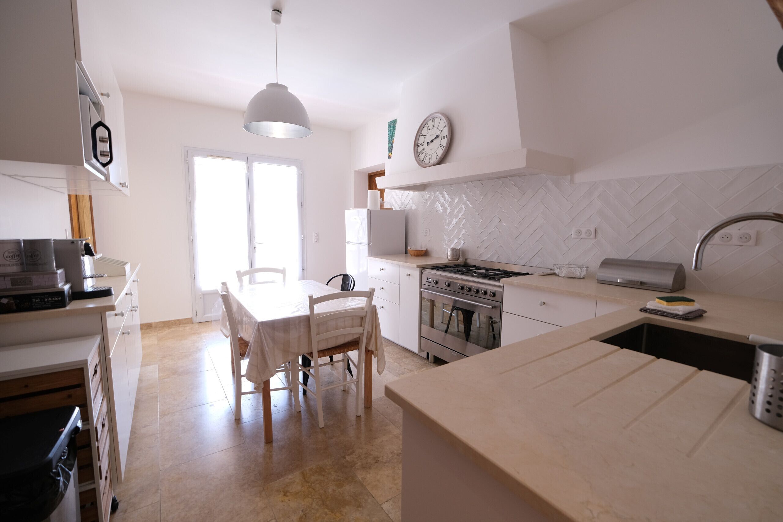 Una cocina moderna con armarios blancos, una mesa de comedor, sillas, estufa y lavaplatos.