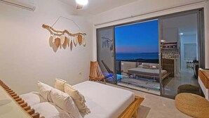 Un dormitorio con cama, ventilador de techo y vista al mar a través de una puerta corrediza de vidrio.