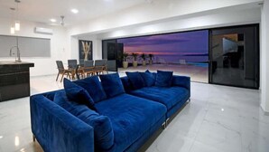 Una sala de estar moderna con un sofá azul, un comedor y un amplio ventanal con vista al atardecer.