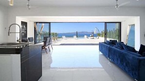 Un interior moderno con cocina, comedor y un amplio ventanal corredero que da a un patio con vistas al mar.