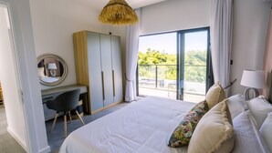 A bedroom with a large bed, a desk, a wardrobe, and a balcony with a view of greenery. - Pearl Villa (Grand-Baie)