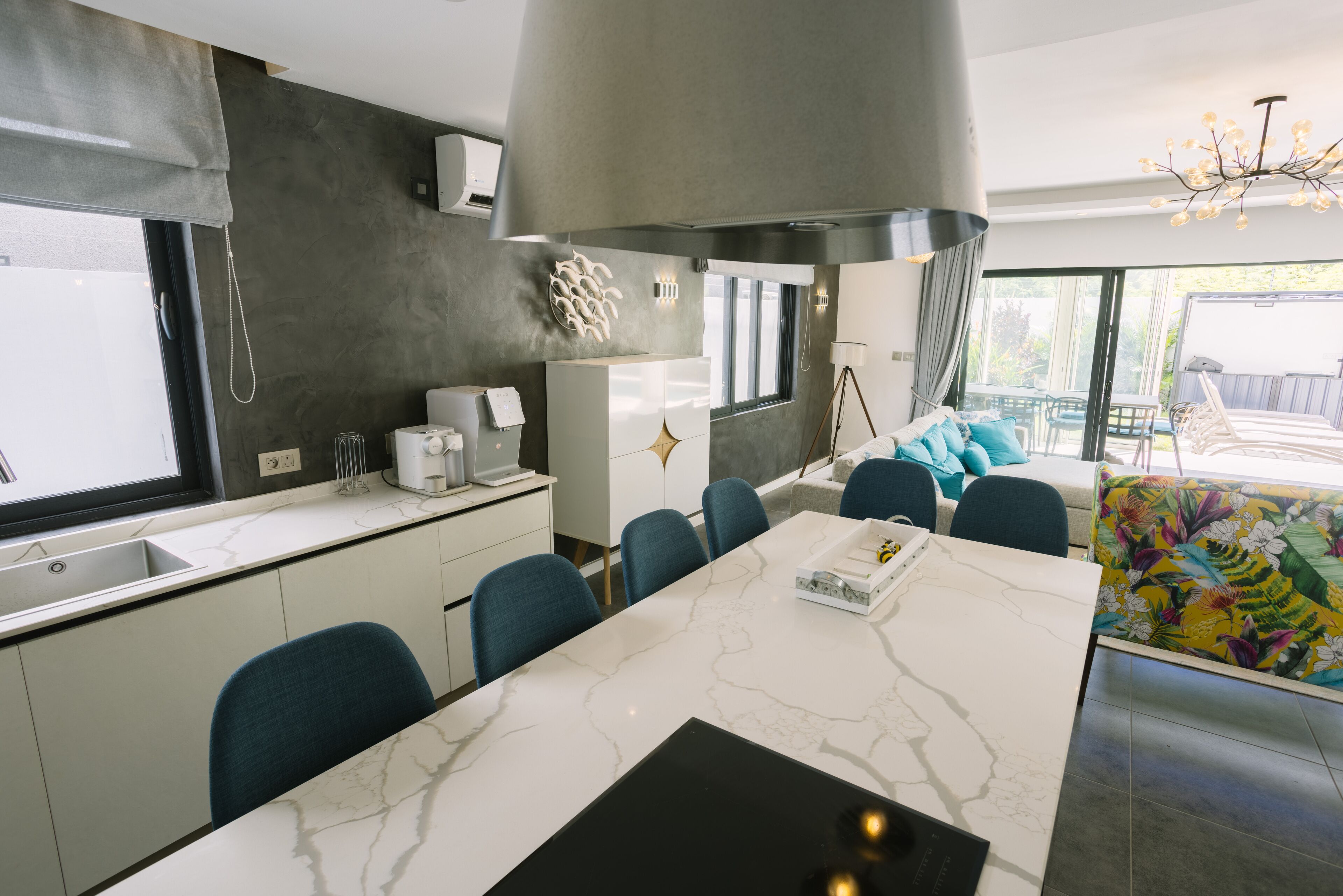 Een moderne keuken met een marmeren aanrecht, een zithoek met blauwe stoelen en een groot raam.