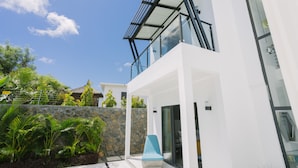 A modern building with a glass balcony, stone wall, and tropical plants. - Pearl Villa (Grand-Baie)