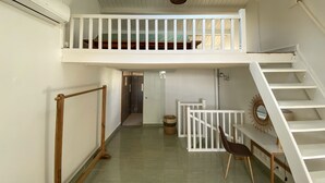 A spacious room with a high ceiling, a skylight, a balcony, a staircase, and a small table with a chair. - Appart Standing vue mer & Marina (Pointe-à-Pitre)